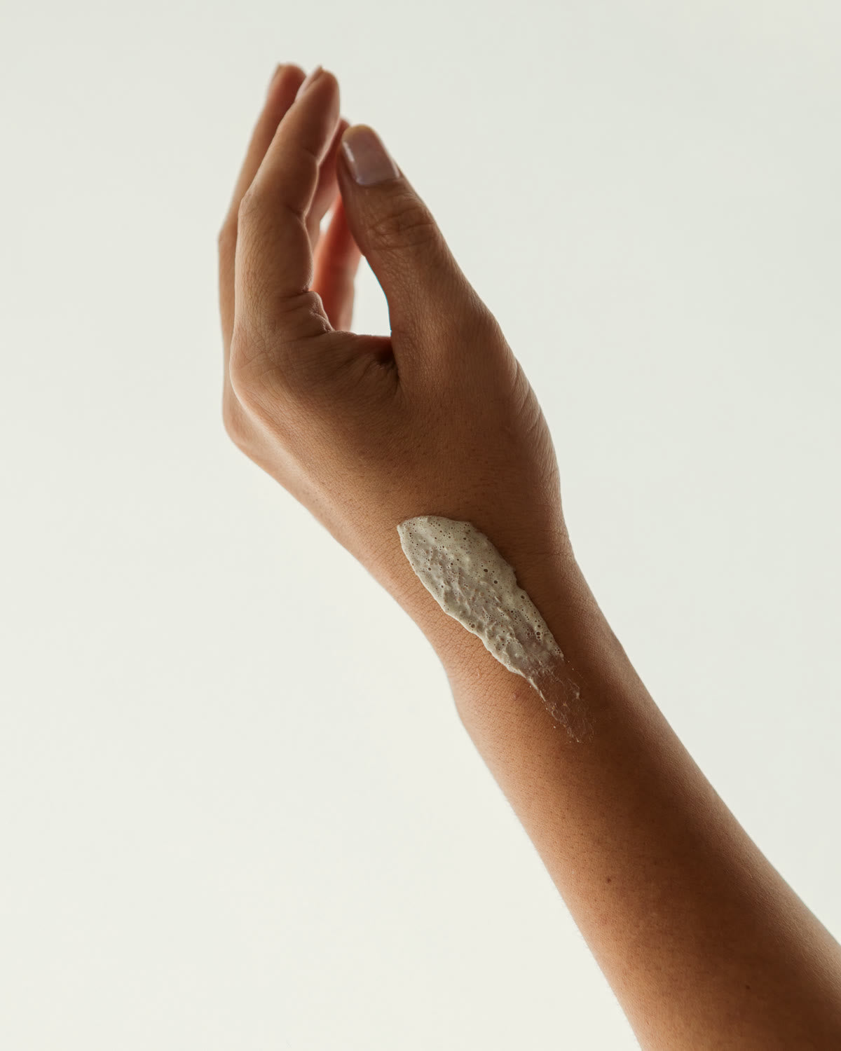 Mão em gesto leve com a argila do Grão Esfoliante aplicada no pulso